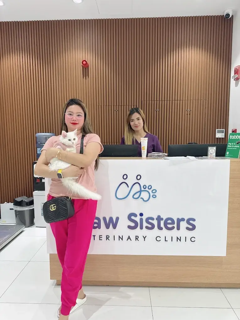 عميلة مبتسمة من Paw Sisters تحمل قطتها البيضاء في العيادة بالقرهود، دبي